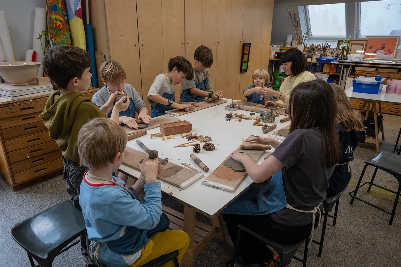 A group of children around a table in an art room working with clay, pine cones and leaves