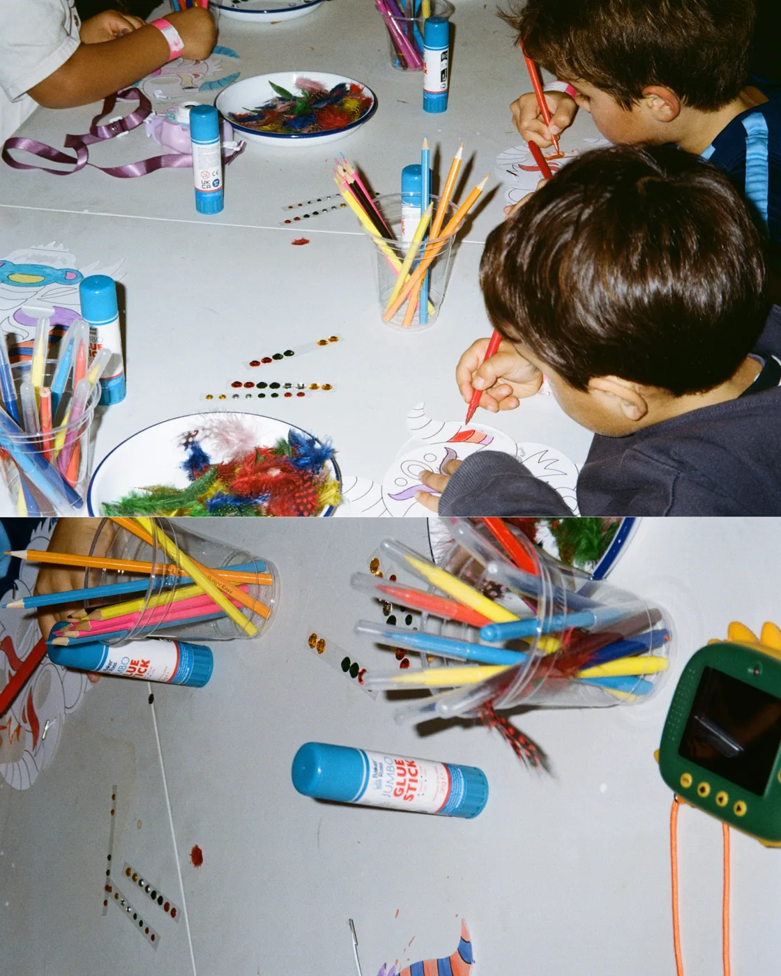 Children drawing with felt-tip pens and crayons at a table covered in paper, glue sticks and pots of pens