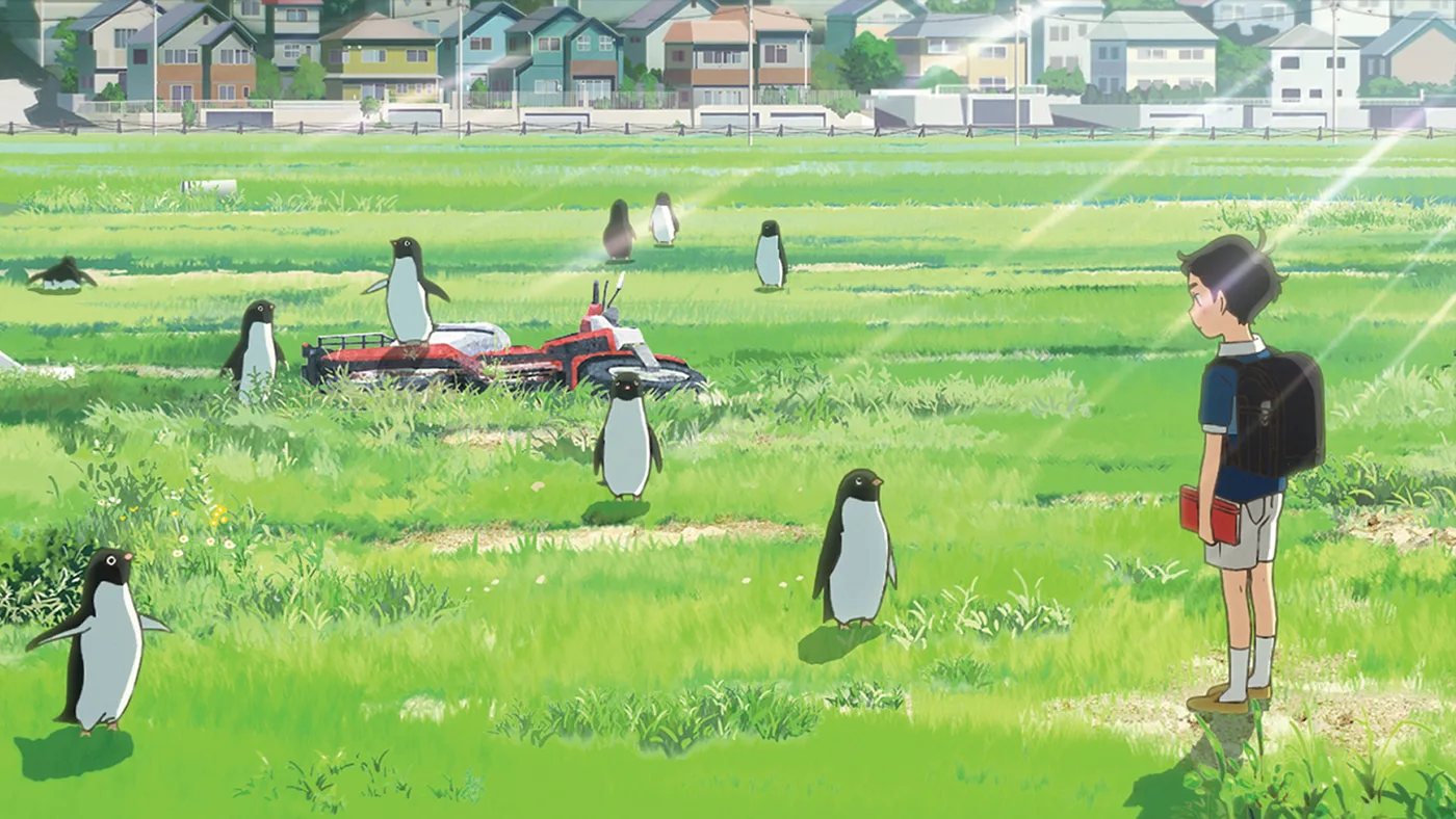 Anime still of a boy with a backpack standing in a green field watching several penguins, with houses behind