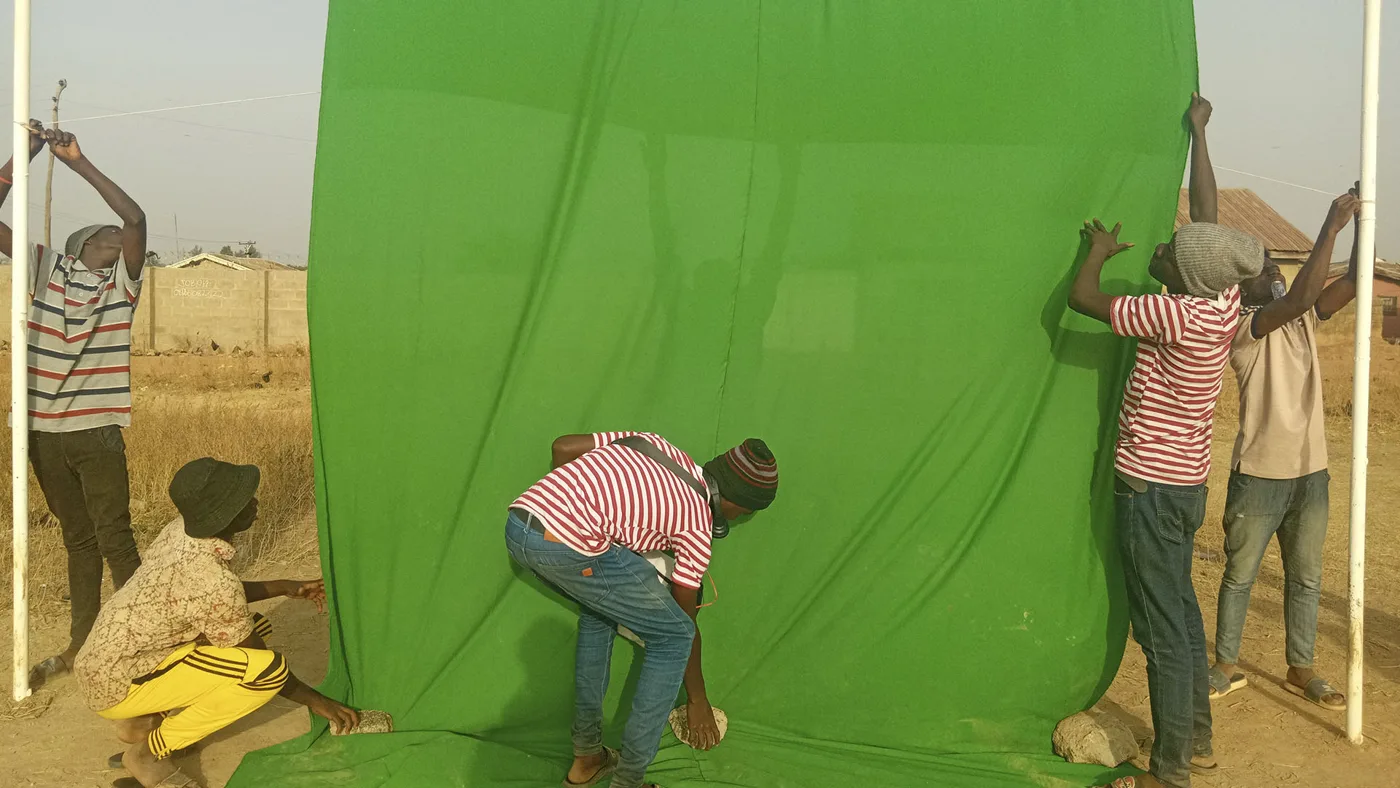Young people hanging a large green sheet between poles outdoors on dry, dusty ground